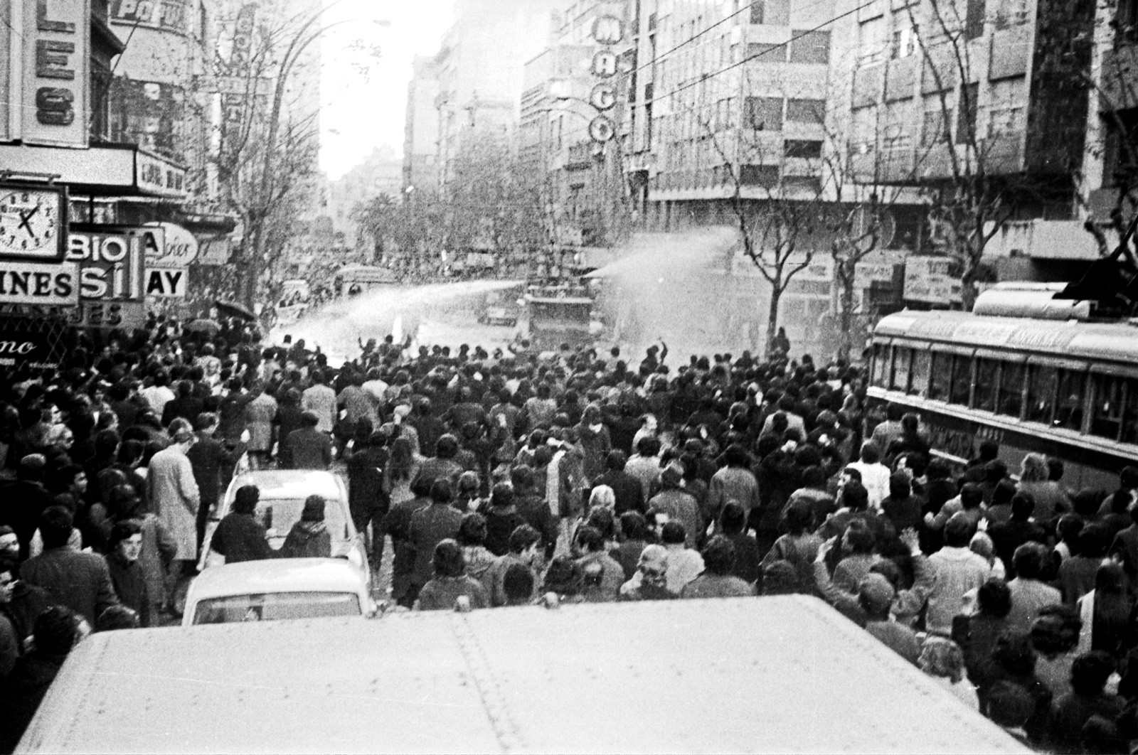 Manifestación durante la huelga general. Avenida 18 de Julio y Río Branco, Montevideo. En las fotos se aprecia el cartel de la tienda El Mago, el del Diario El Popular ubicado enfrente y el reloj indicando la hora; un carro lanza agua - conocido como autobomba o guanaco -. 27 de junio - 11de julio de 1973. Foto Aurelio González -cdf